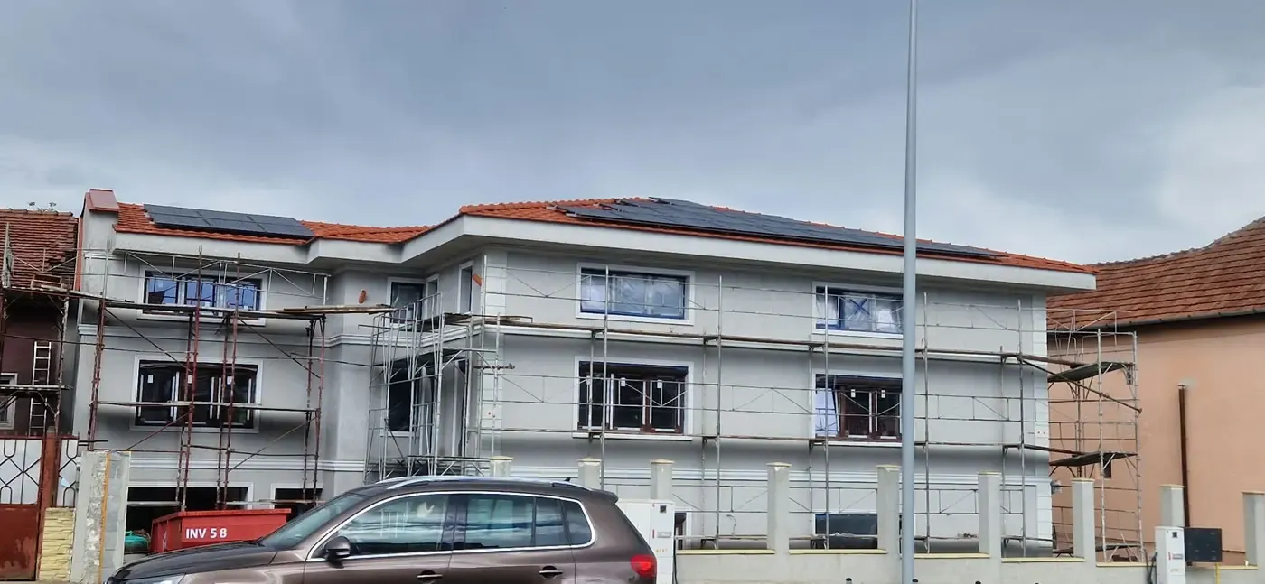 Clădire în construcție, cu schele pe fațadă și panouri fotovoltaice pe acoperiș