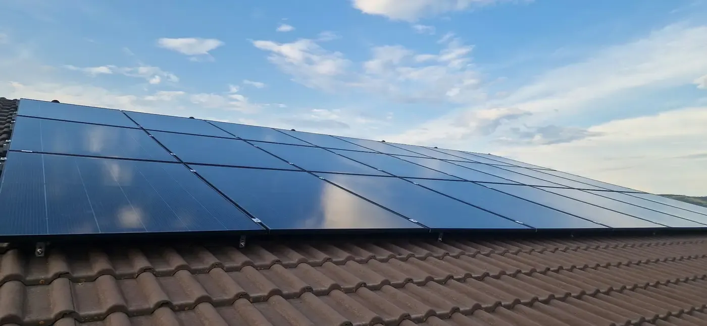 Panouri fotovoltaice negre pe un acoperiș de țiglă, sub un cer albastru cu nori albi