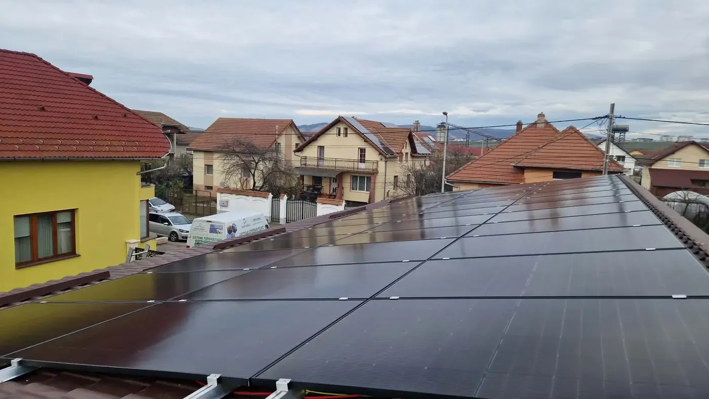 Panouri fotovoltaice negre pe un acoperiș, cu o stradă și case cu acoperișuri roșii în fundal