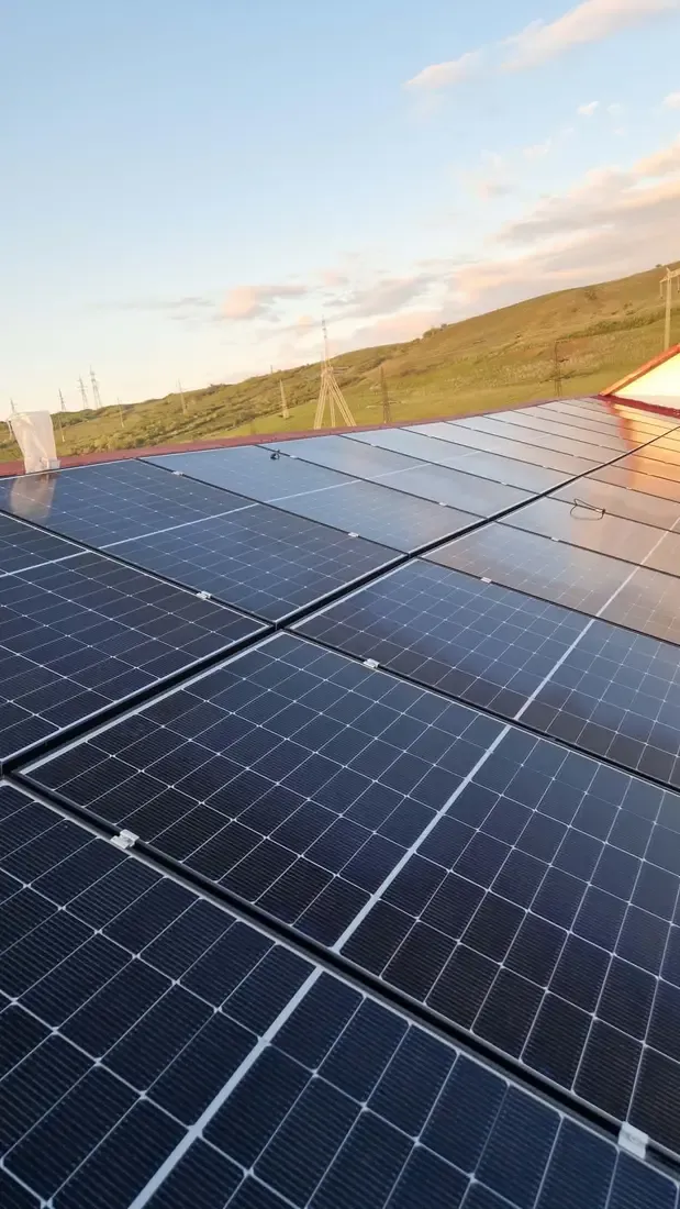 Panouri fotovoltaice văzute de aproape, cu un deal verde în fundal