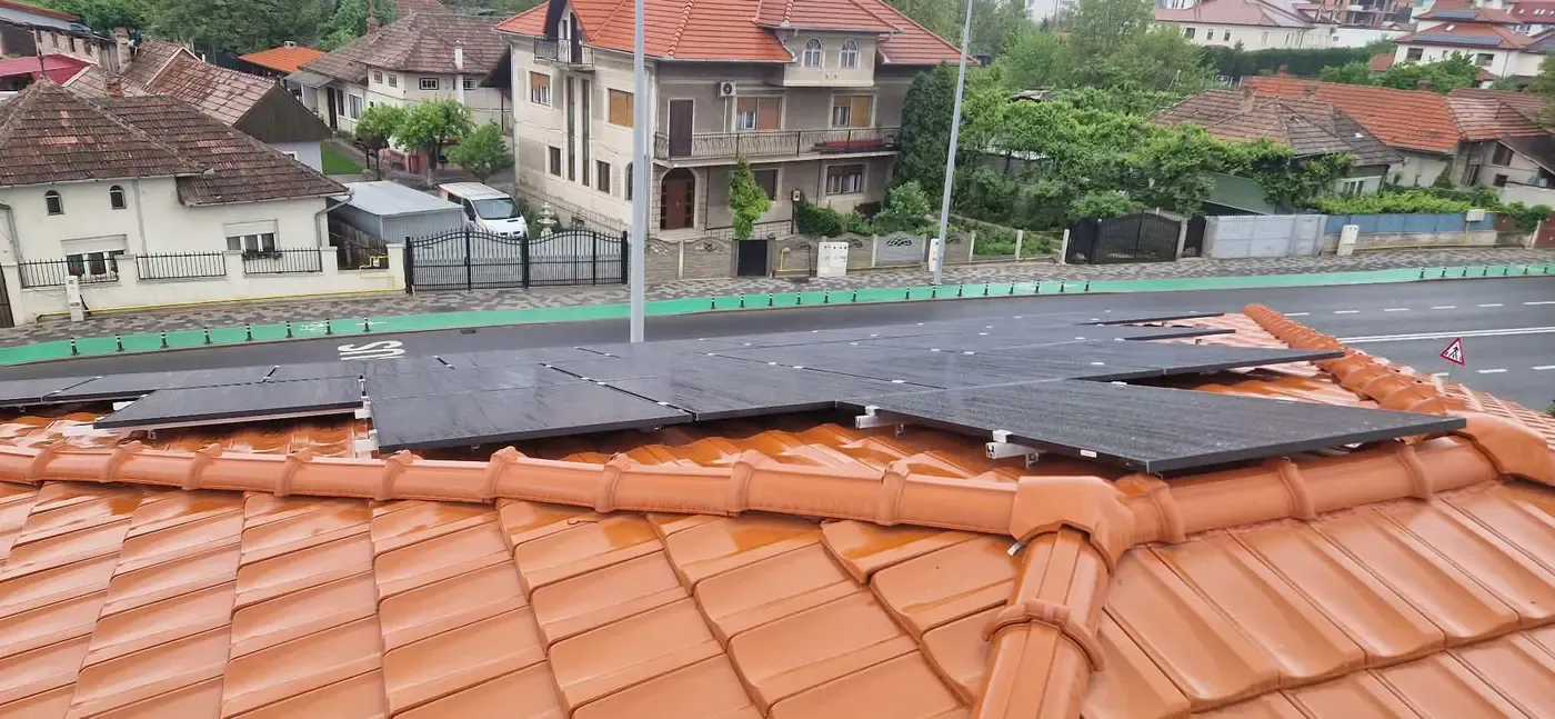 Panouri fotovoltaice negre pe un acoperiș de țiglă ceramică portocalie, în fața unei străzi